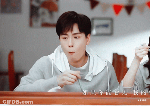 A Man Sitting At A Table With Chinese Writing On The Wall Behind Him GIF
