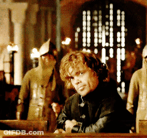 A Man Sitting At A Table With His Arms Crossed Looking At The Camera GIF