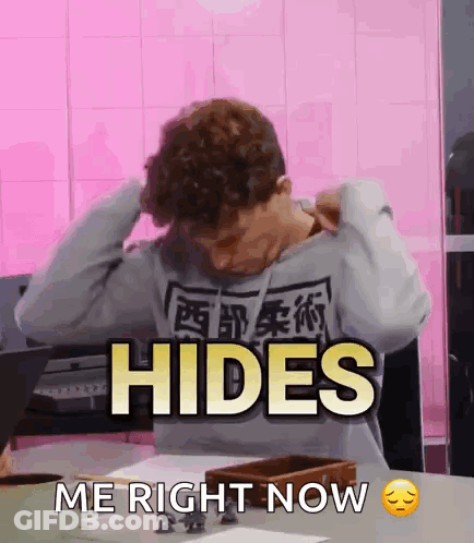 A Man Sitting At A Table With His Hands On His Head And The Words Hides Me Right Now GIF