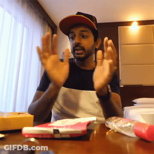 A Man Sitting At A Table With His Hands Up GIF