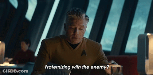 A Man Sitting At A Table With The Words " Fraternizing With The Enemy " Below Him GIF
