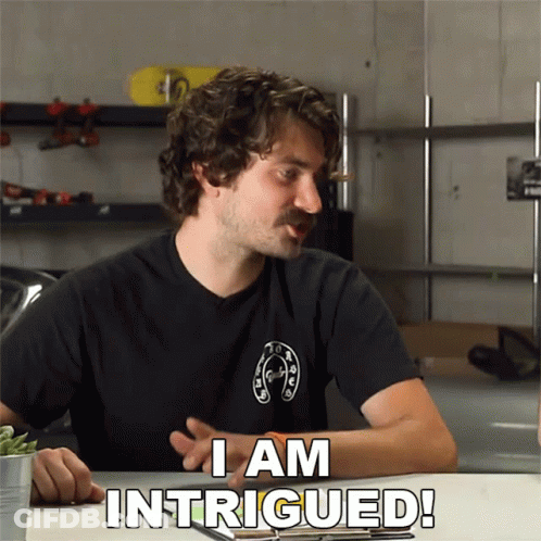 A Man Sitting At A Table With The Words I Am Intrigued GIF