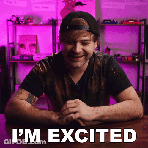 A Man Sitting At A Table With The Words " I 'M Excited " Written On The Screen GIF
