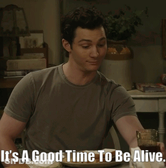 A Man Sitting At A Table With The Words It 'S A Good Time To Be Alive On The Bottom GIF