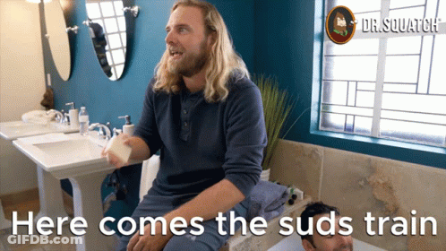A Man Sitting In A Bathroom With The Words Here Comes The Suds Train On The Bottom GIF