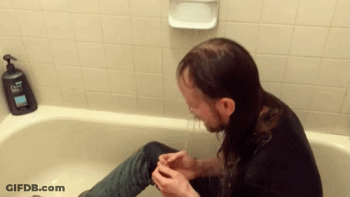 A Man Sitting In A Bathtub With A Dove Soap Dispenser On The Wall Behind Him GIF
