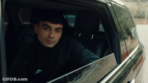 A Man Sitting In A Car With The Word Adidas On His Shirt GIF