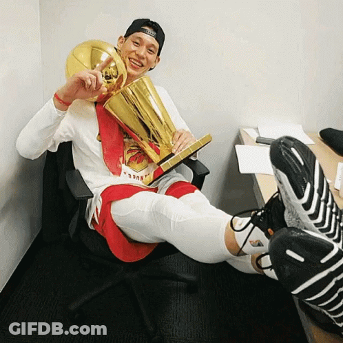 A Man Sitting In A Chair Holding A Trophy That Says ' Nba ' On It GIF