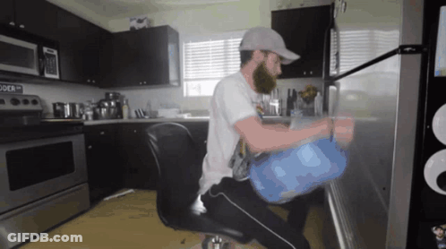 A Man Sitting In A Chair In A Kitchen With A Microwave That Says " Powder " On It GIF