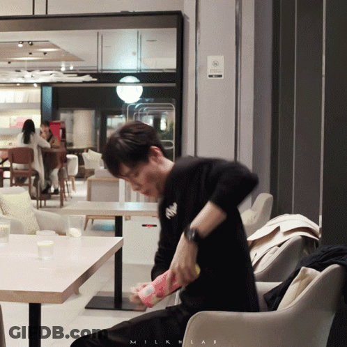 A Man Sitting In A Chair In Front Of A Sign That Says Milklab GIF