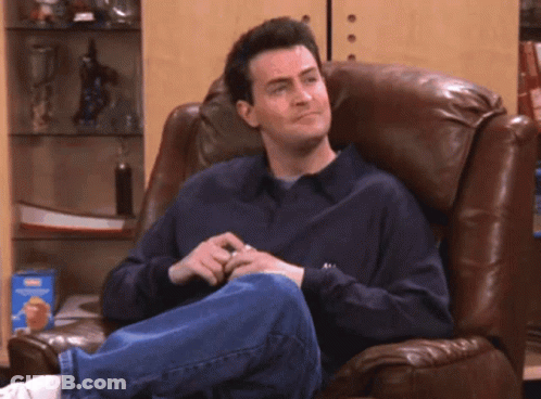A Man Sitting In A Chair Laughing With His Mouth Open GIF