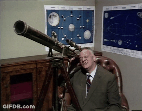 A Man Sitting In A Chair Looking Through A Telescope With Posters On The Wall Behind Him GIF