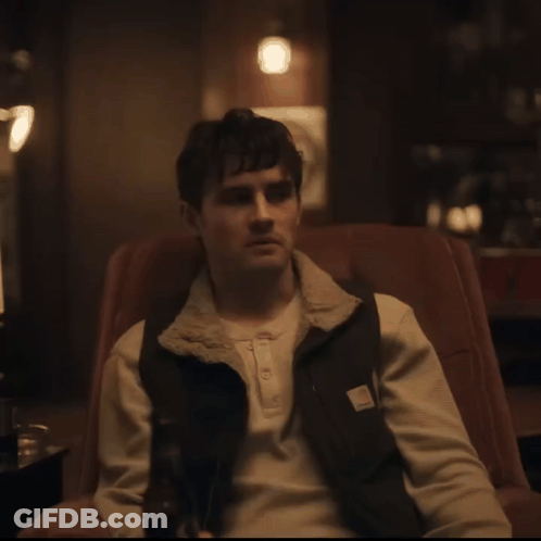 A Man Sitting In A Chair Wearing A Carhartt Vest GIF