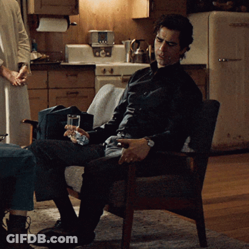 A Man Sitting In A Chair With A Glass Of Water In His Hand GIF