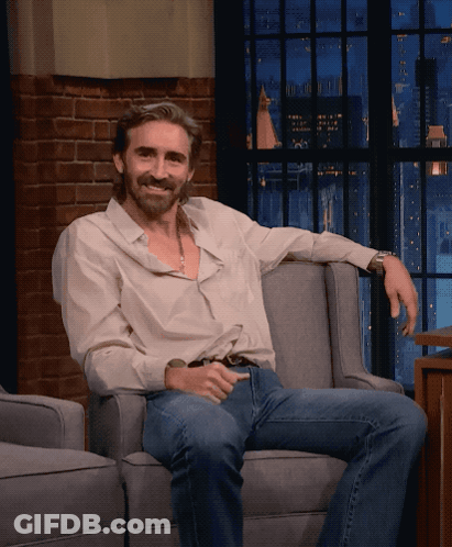A Man Sitting In A Chair With His Arm Resting On The Arm Rest GIF