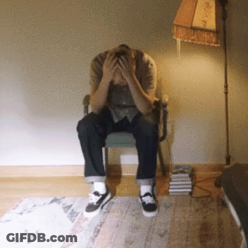 A Man Sitting In A Chair With His Hands On His Head GIF