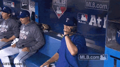 A Man Sitting In A Dugout Talking On A Phone With Mlb.com Written On The Wall Behind Him GIF