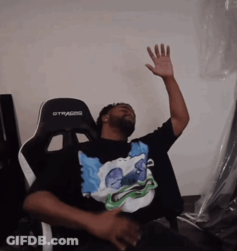 A Man Sitting In A Gtracing Chair With His Hand Up In The Air GIF