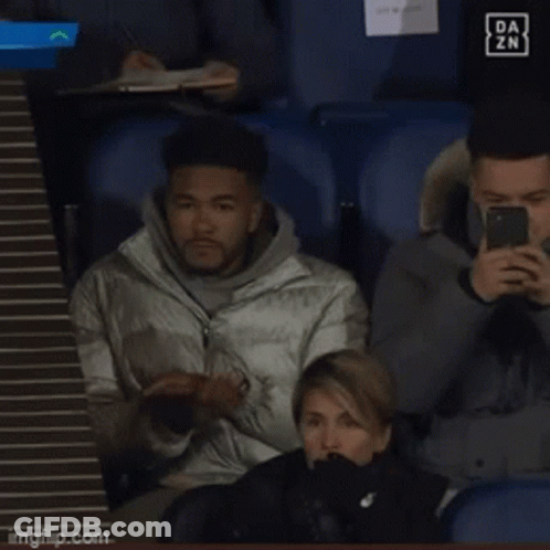 A Man Sitting In A Stadium Looking At His Phone With A Da Zn Logo In The Background GIF