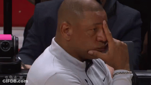 A Man Sitting In A Stadium With His Hand On His Face GIF