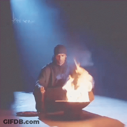 A Man Sitting In Front Of A Bowl Of Fire With Smoke Coming Out Of It GIF