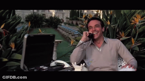 A Man Sitting In Front Of A Briefcase Talking On A Telephone GIF
