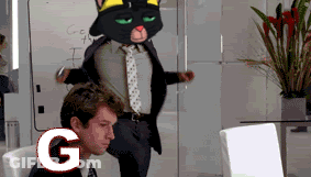A Man Sitting In Front Of A Computer With A Cat Mascot Behind Him With The Letter G In The Foreground GIF