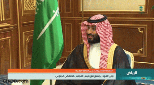 A Man Sitting In Front Of A Green And White Flag With The Words " الرياض " On The Bottom GIF