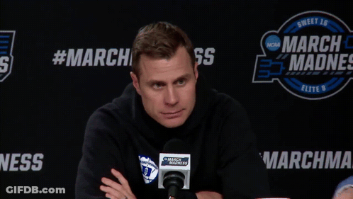 A Man Sitting In Front Of A March Madness Banner GIF