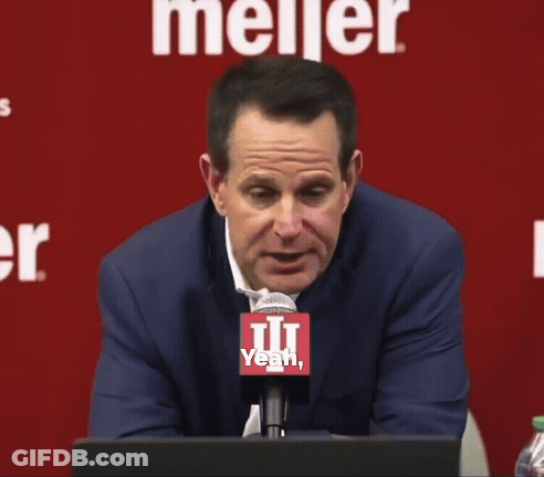 A Man Sitting In Front Of A Meijer Sign Talking Into A Microphone GIF