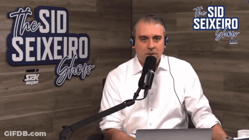 A Man Sitting In Front Of A Microphone In Front Of A Sign That Says The Sid Seixeiro Show GIF
