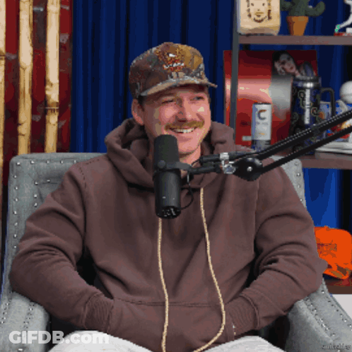 A Man Sitting In Front Of A Microphone Wearing A Hat That Says ' Abercrombie & Fitch ' On It GIF