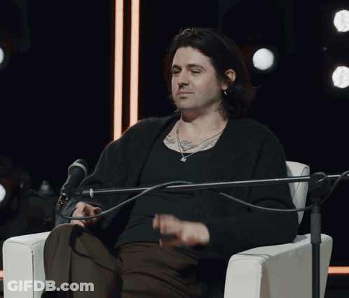 A Man Sitting In Front Of A Microphone With A Tattoo On His Arm GIF