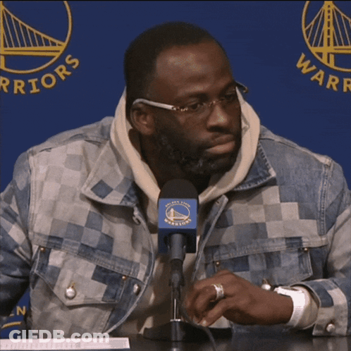 A Man Sitting In Front Of A Microphone With The Golden State Warriors Logo Behind Him GIF