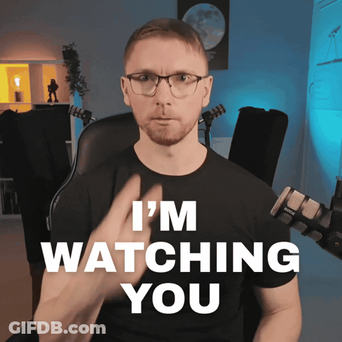 A Man Sitting In Front Of A Microphone With The Words I 'M Watching You Behind Him GIF