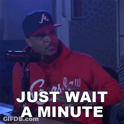 A Man Sitting In Front Of A Microphone With The Words Just Wait A Minute Written Below Him GIF