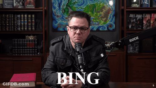 A Man Sitting In Front Of A Rode Microphone With The Word Bing On The Screen GIF