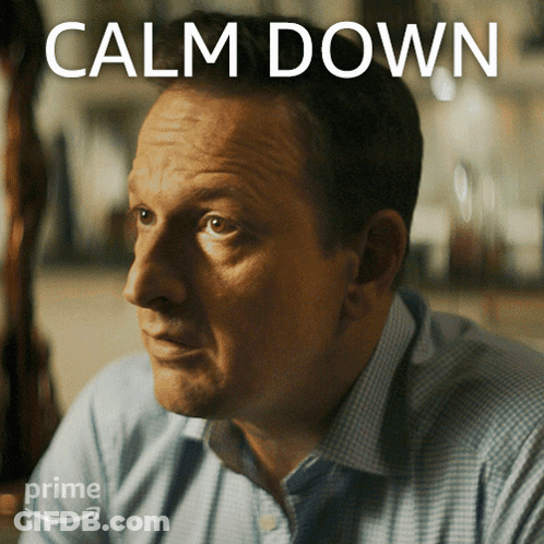 A Man Sitting In Front Of A Sign That Says " Calm Down " GIF