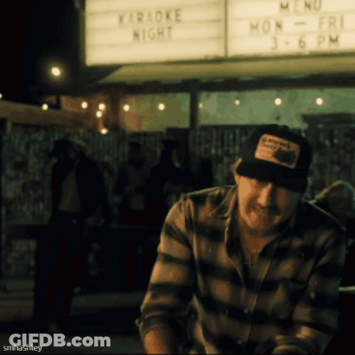 A Man Sitting In Front Of A Sign That Says " Karaoke Night " GIF