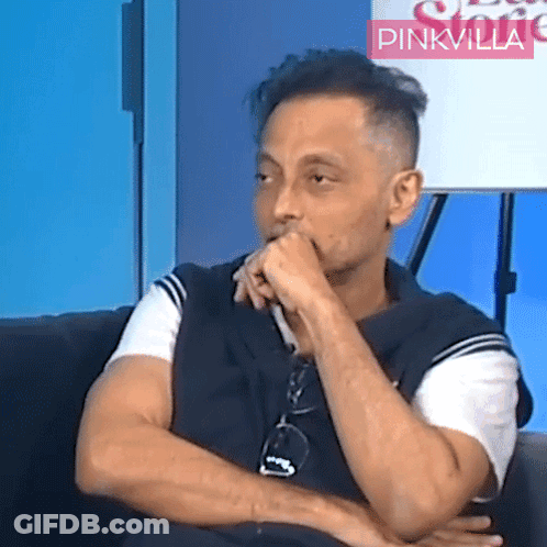 A Man Sitting In Front Of A Sign That Says Pinkvilla On It GIF
