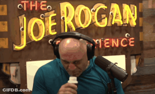 A Man Sitting In Front Of A Sign That Says The Joe Rogan Fence GIF