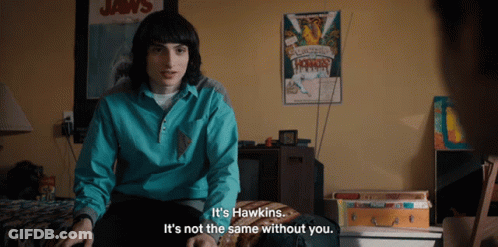 A Man Sitting On A Bed With A Poster On The Wall That Says Jaws GIF