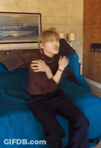 A Man Sitting On A Bed With His Arms Around His Shoulder GIF