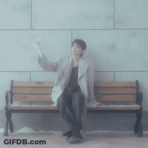 A Man Sitting On A Bench With His Hand Up GIF