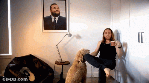 A Man Sitting On A Chair Next To A Dog Holding A Coffee Mug GIF