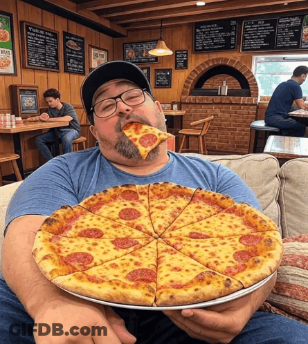 A Man Sitting On A Couch Eating A Large Pizza GIF
