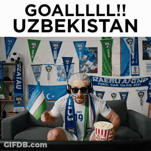 A Man Sitting On A Couch Holding A Bag Of Popcorn And Wearing A Scarf That Says Ufa GIF