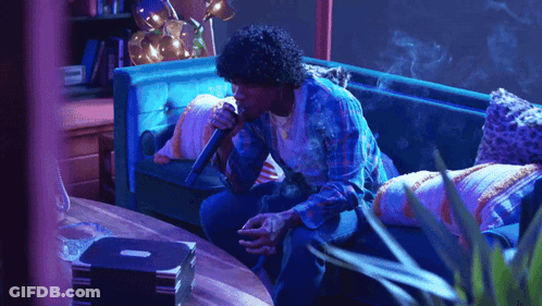 A Man Sitting On A Couch Holding A Microphone GIF
