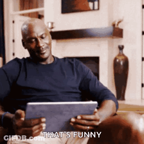 A Man Sitting On A Couch Looking At A Tablet With The Words That 'S Funny Below Him GIF