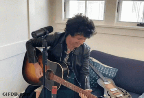 A Man Sitting On A Couch Playing A Guitar GIF